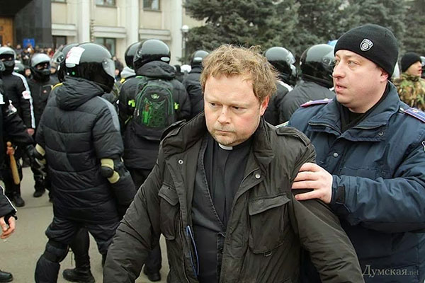 Rev. Andreas Hamburg is pulled away from the violence by a police officer. (Photo from a Dumskaya report on the assault on the protesters.